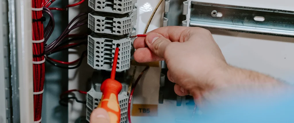 A close-up view of a student’s hands as they carefully connect a red wire to an electrical terminal using a screwdriver. The control panel is filled with neatly organized wiring, structured components, and labeled connections, reflecting precision and attention to detail. This hands-on lab setting is part of a Mechanical Engineering Technology program, where students learn about automation, electrical systems, and mechanical design, preparing for careers in manufacturing, robotics, and industrial maintenance.