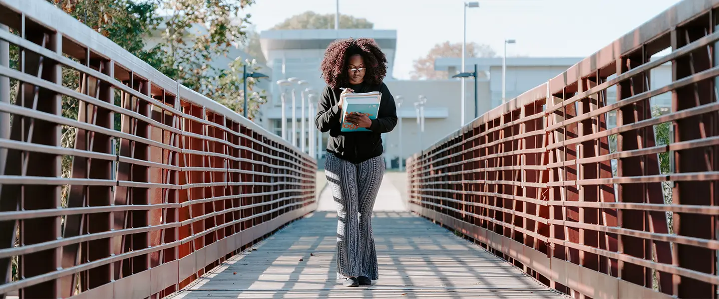 Student walking confidently across a red pedestrian bridge on campus.