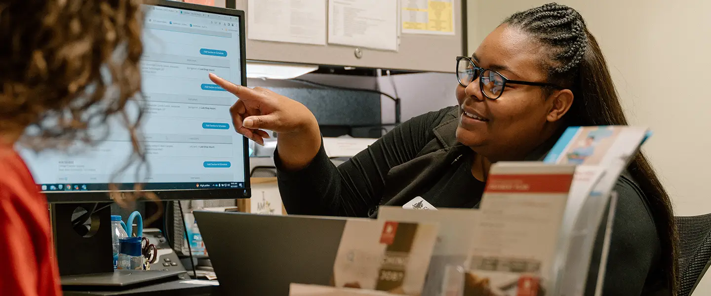 Advisor assisting a student on a computer in a modern workspace.
