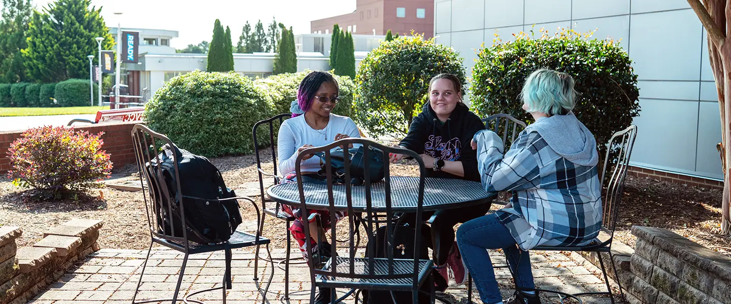 Group of students smiling together at an outdoor campus table.