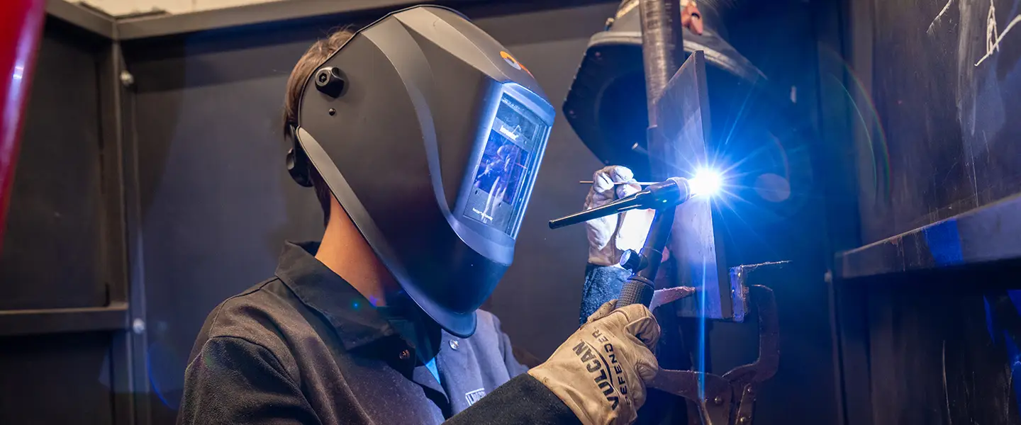Student welding with safety gear in a technical lab.