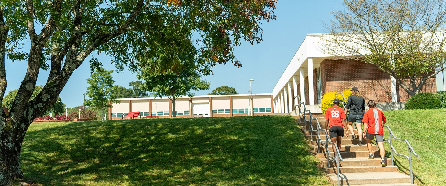 Image of 3 male students in athletic attire walking away from the camera up stairs in the right of the photo to the CVCC Quad