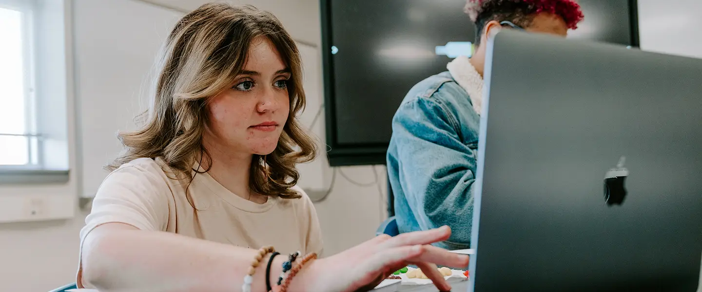Student working on a computer and listening during classroom discussion.