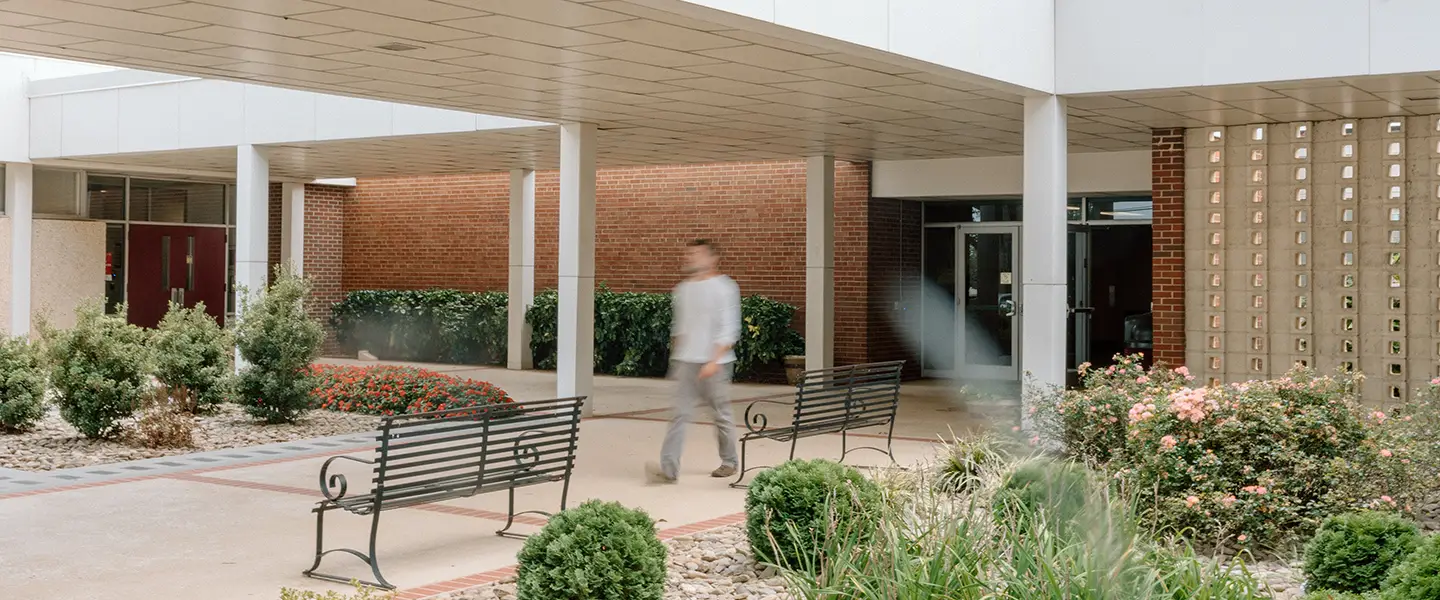 Student walking across a quiet landscaped courtyard near a CVCC building.